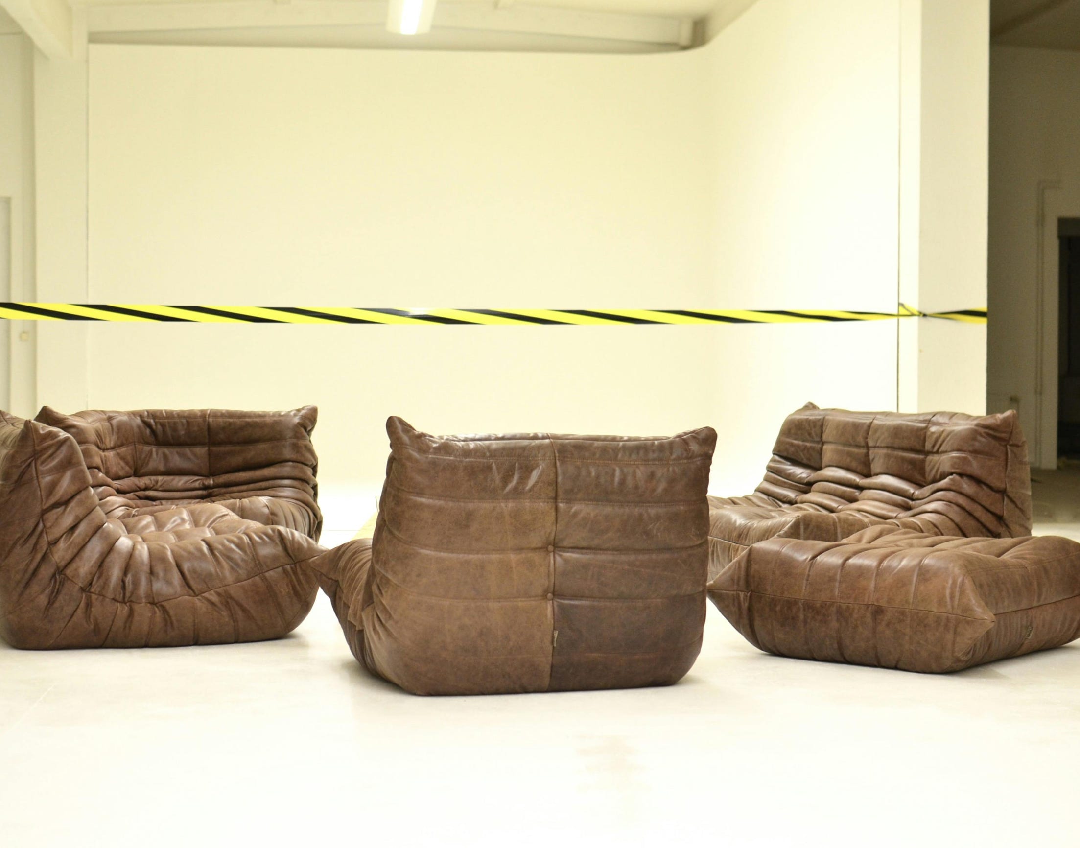 Leather couches placed in empty room under bright striped barrier tape during renovation process