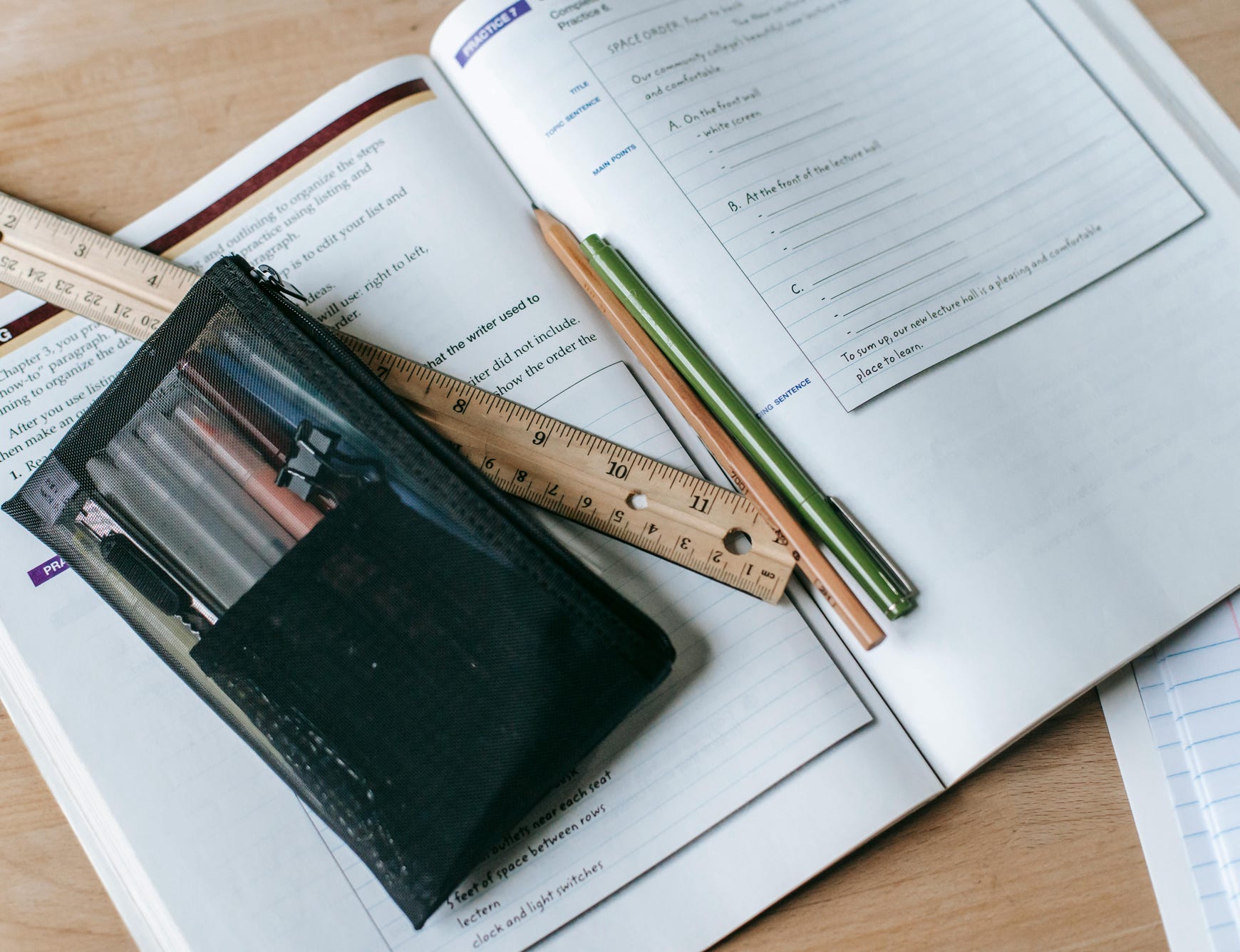 From above of textbook with exercises and ruler with pens near small case on table