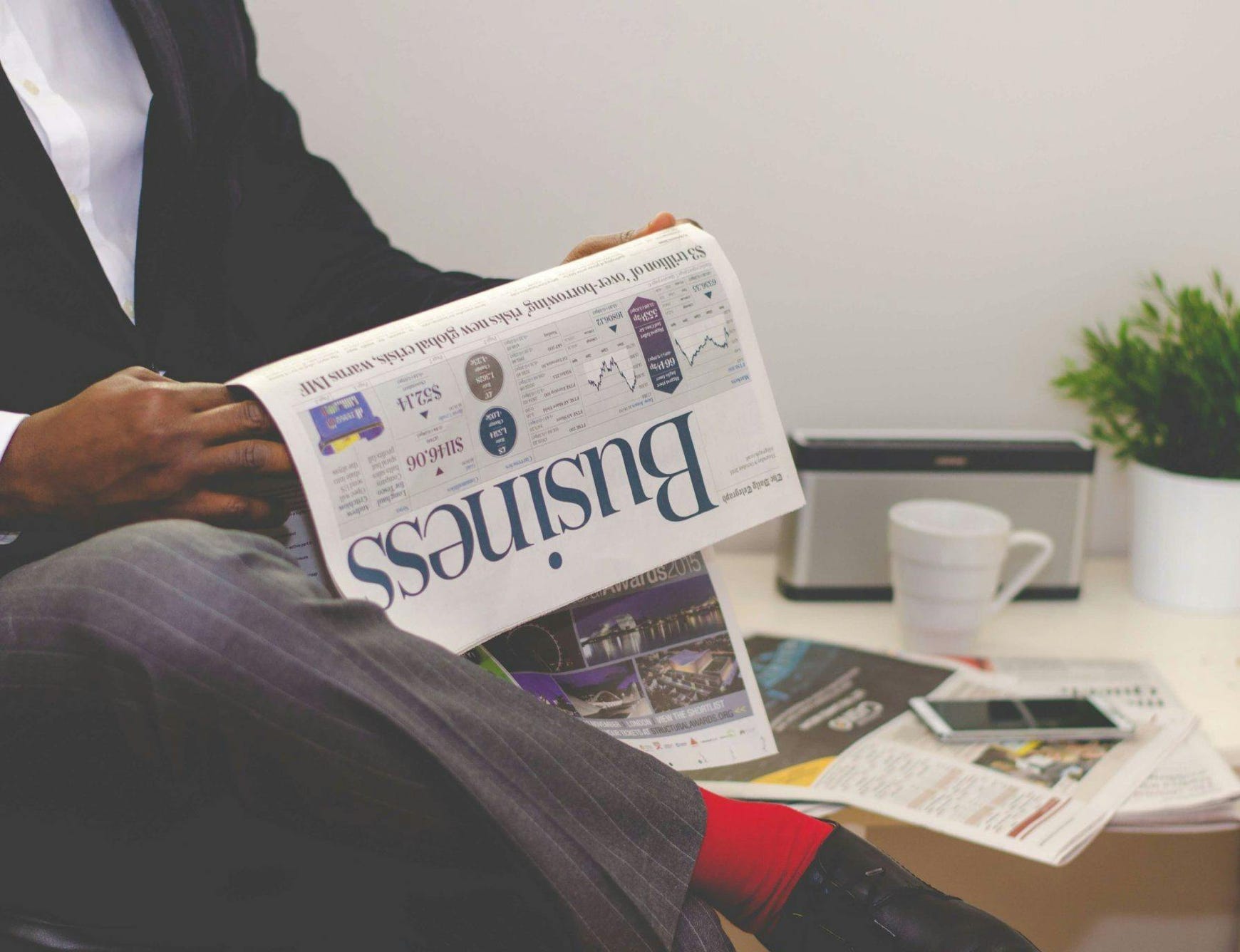 Man Reading Newspaper While Sitting Near Table With Smartphone and Cup